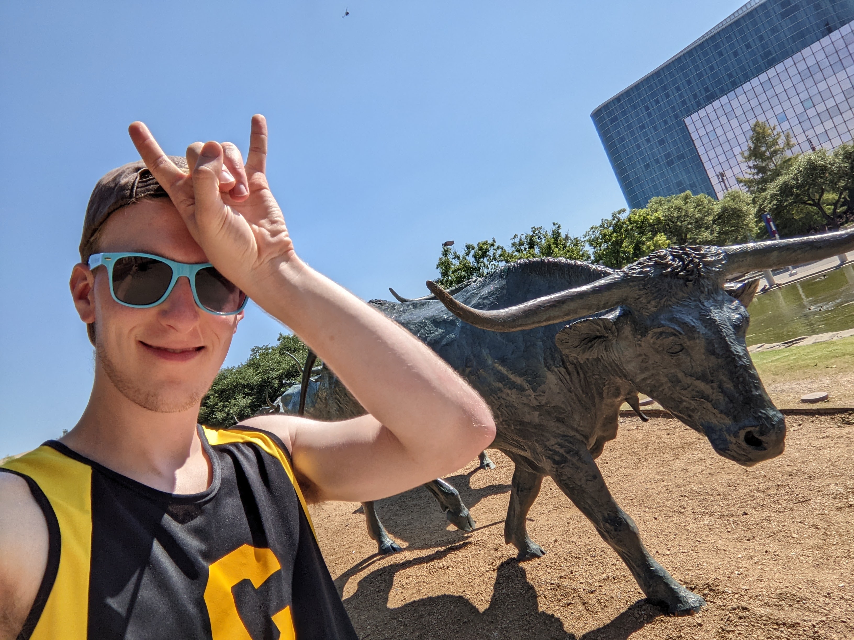 Kyle showing the "hook 'em horns" in front of a Brass Texas Longhorn statue